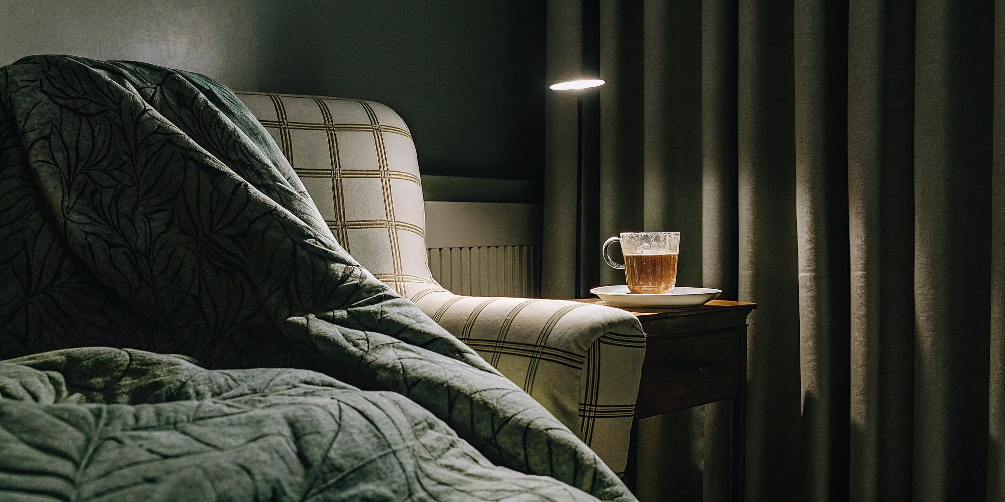 A cozy weighted blanket on a chair next to a warm drink in a calm, softly lit room.