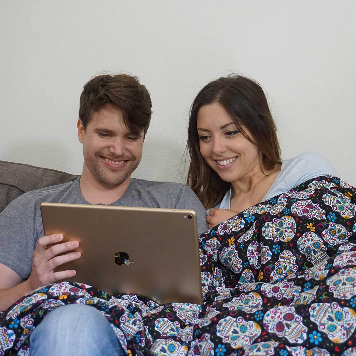 A young couple watches videos on their iPad snuggled under their Dia de los Muertos Weighted Blanket