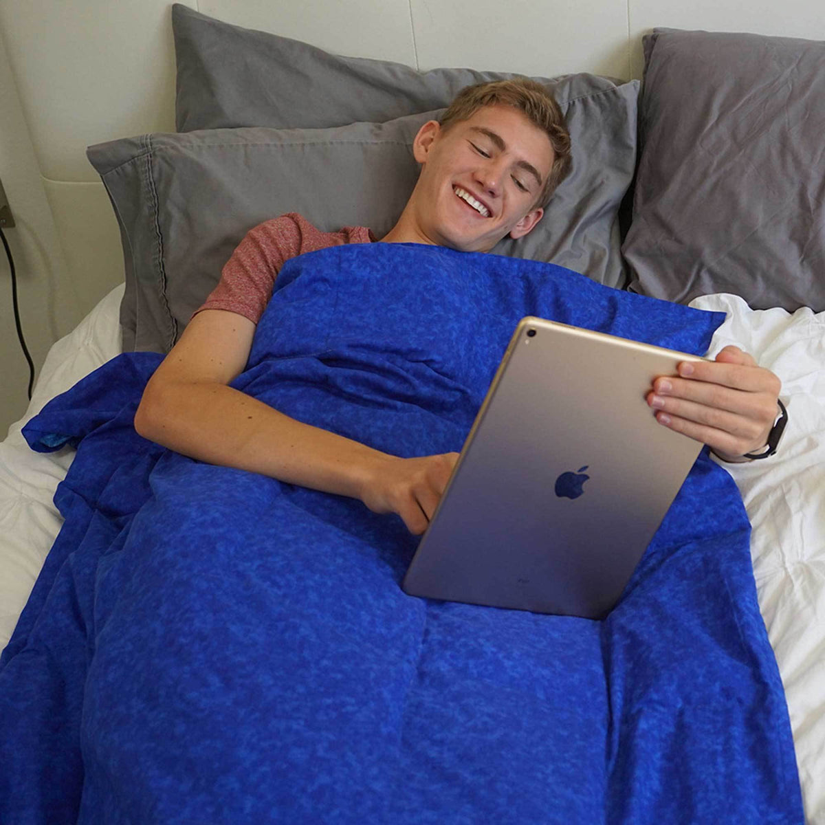 Man reads from his iPad under the covers of his Navy Blue Weighted Blanket in bed