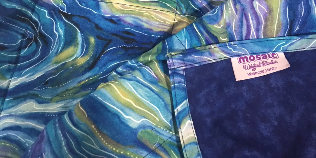 Close-up of a handmade Mosaic Weighted Blanket with vibrant blue and green swirl fabric and a visible Mosaic label, representing custom weighted blanket craftsmanship