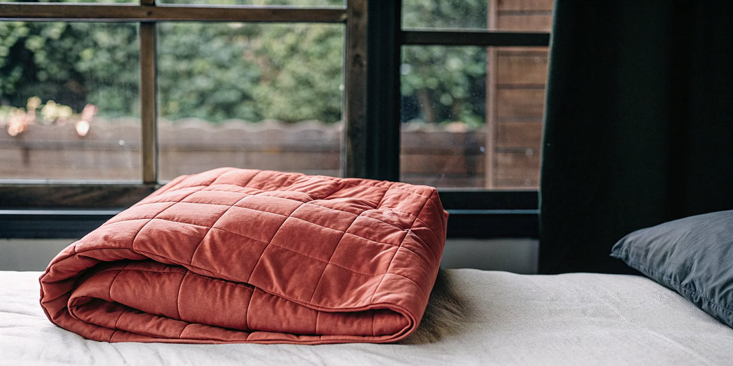 Folded 15 lb weighted blanket on a bed for stress relief and deeper sleep.