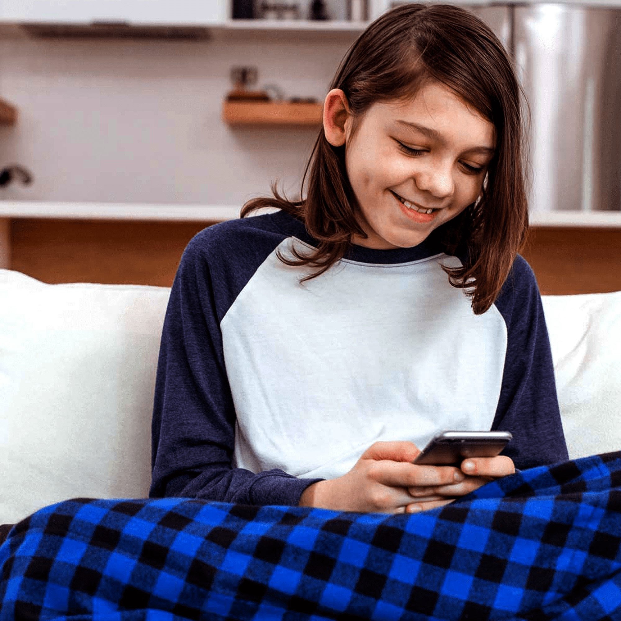 Girl uses her smart phone while snuggles under her Big Blue Flannel Weighted Blanket