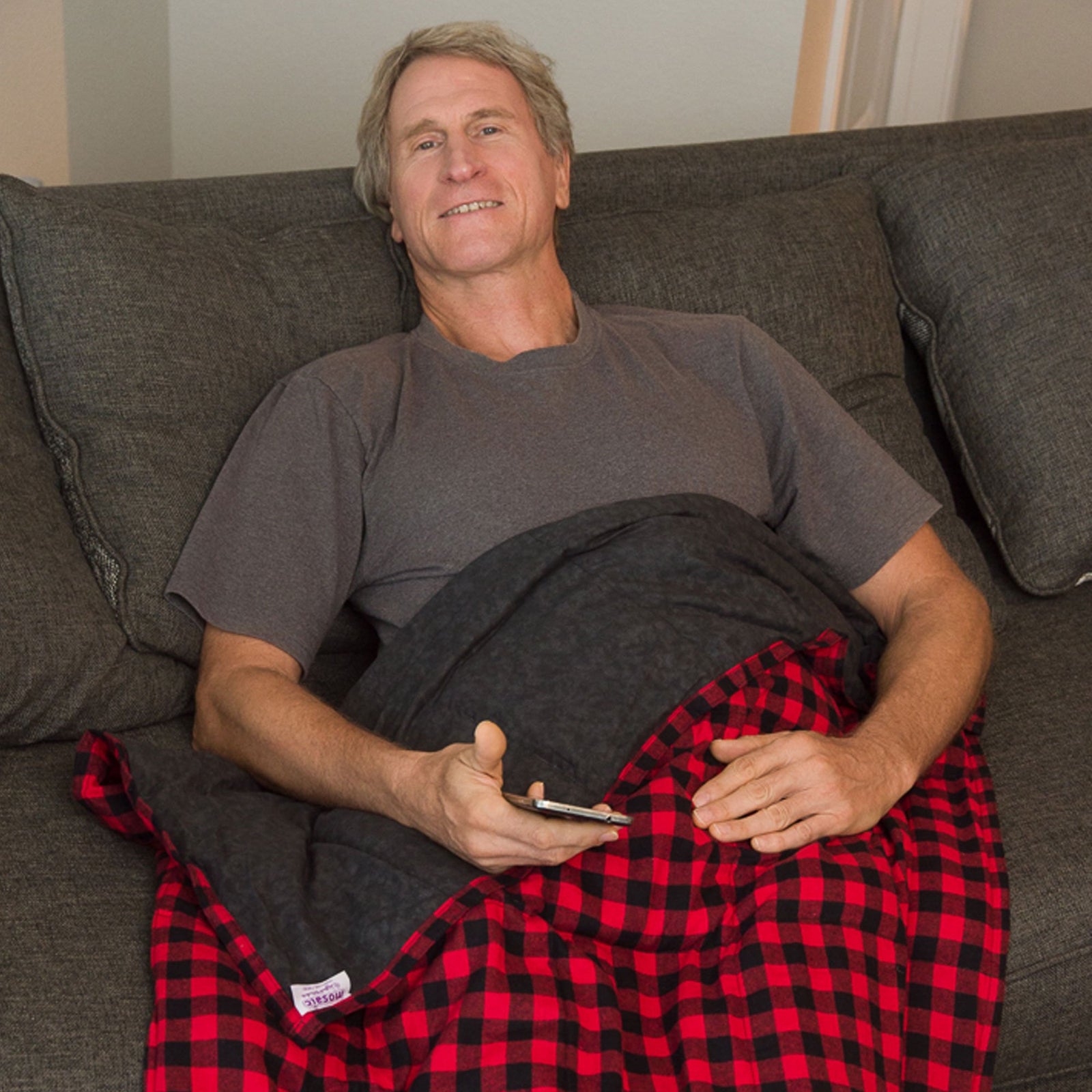 Man watches TV snuggled under a Mosaic Weighted Blankets Big Red Flannel Weighted Blanket