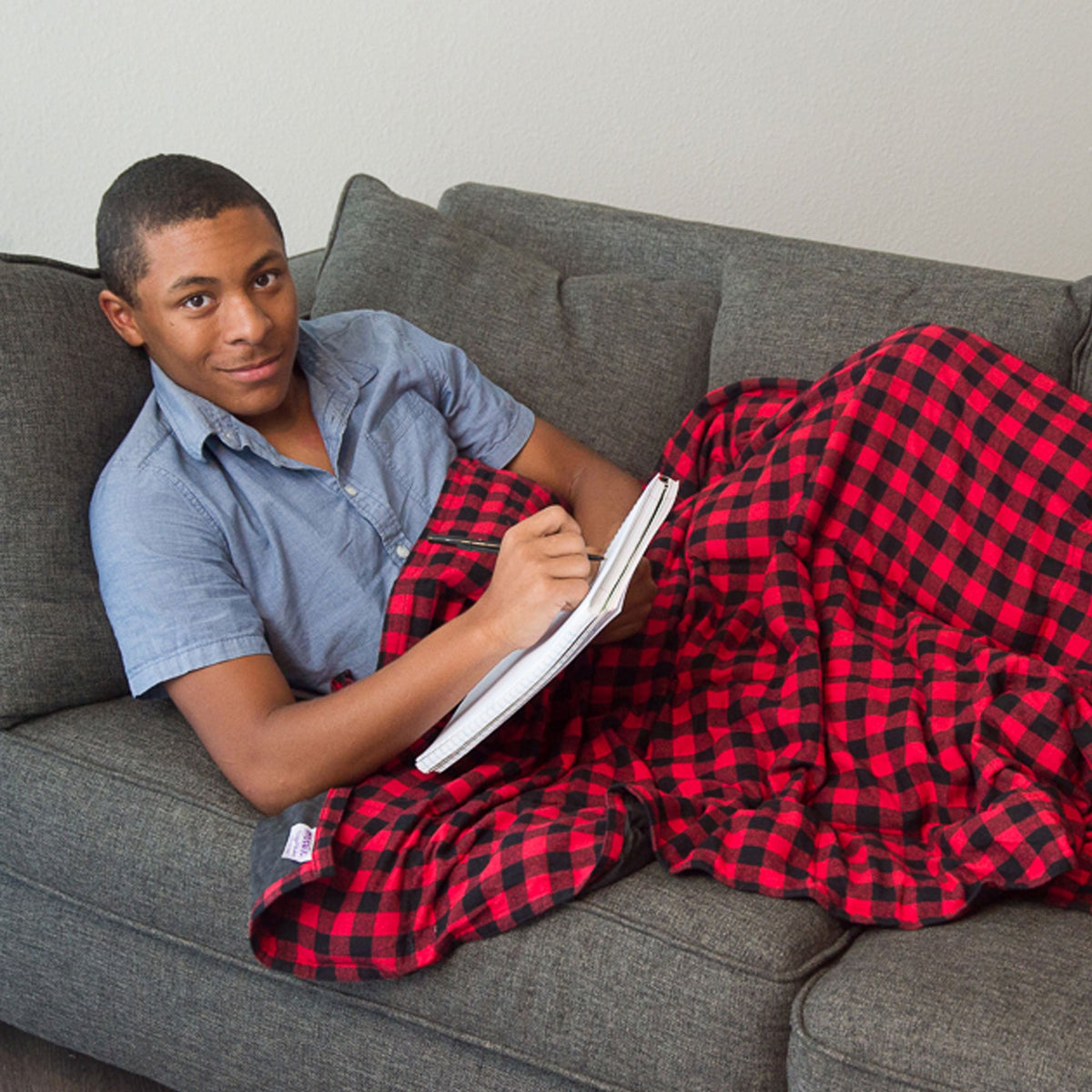 Man reads a hardbound book while snuggled under his Big Red Flannel Weighted Blanket