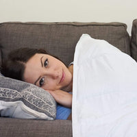 Woman snuggles under her Mosaic Weighted Blankets Blanca White Weighted Blanket on the couch
