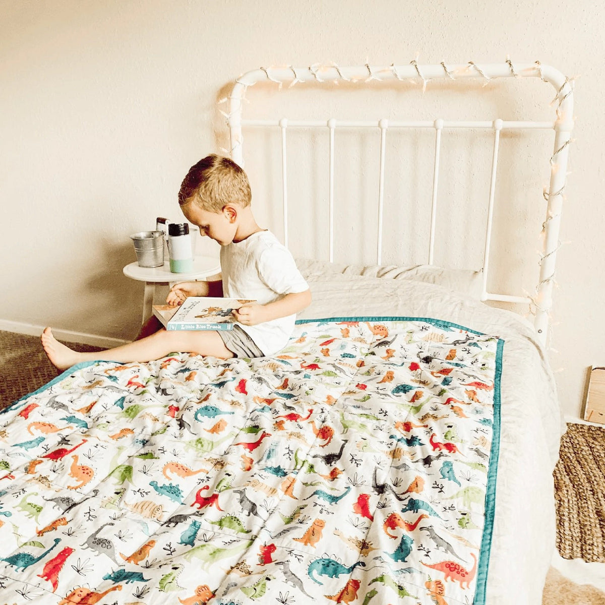 Child sitting on top of Mosaic Weighted Blankets Dinosaur Weighted Blanket on his bed
