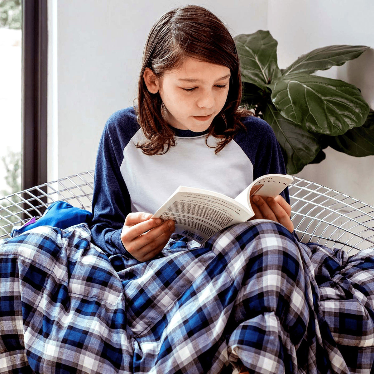 Child Reading And Sitting Under her Blue And White Plaid Weighted Blanket