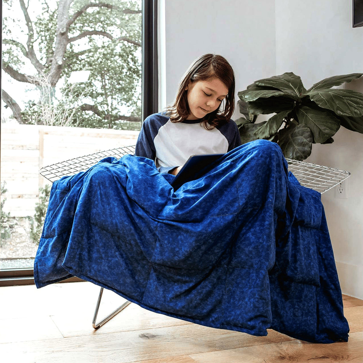 Teen girl reading in a chair under her Mosaic Weighted Blankets Indigo Ocean Waves Weighted Blanket