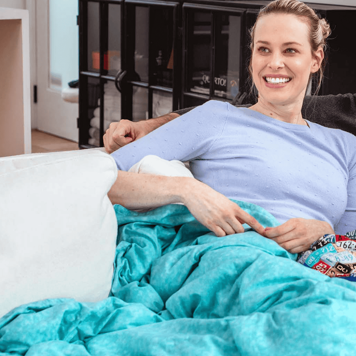 Woman snuggles under her Mosaic Weighted Blankets Light Aqua Weighted Blanket on the couch