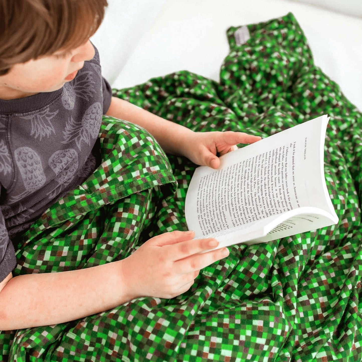 Little boy reads under his Minecraft Cotton Weighted Blanket on his couch