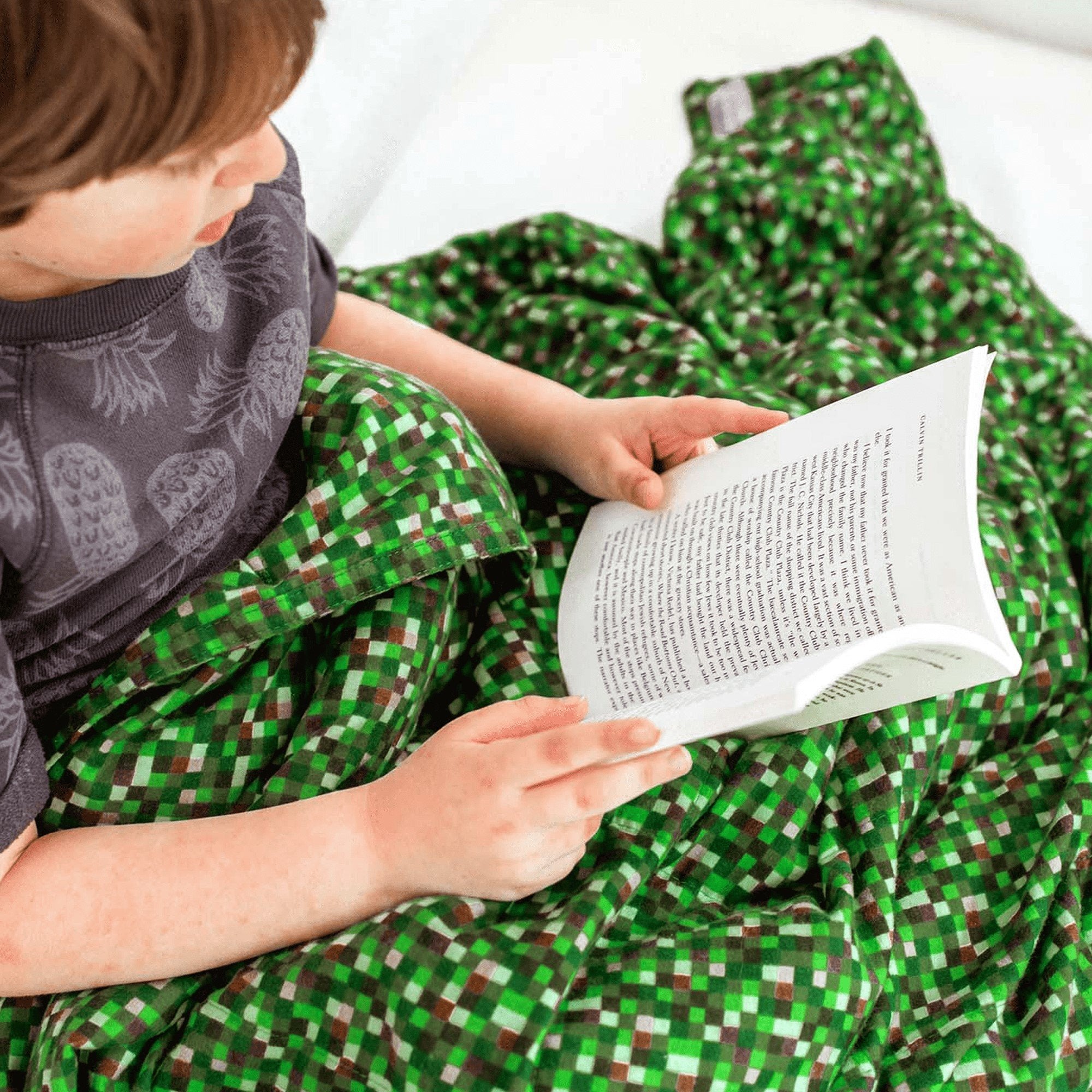 Little boy reads under his Minecraft Cotton Weighted Blanket on his couch