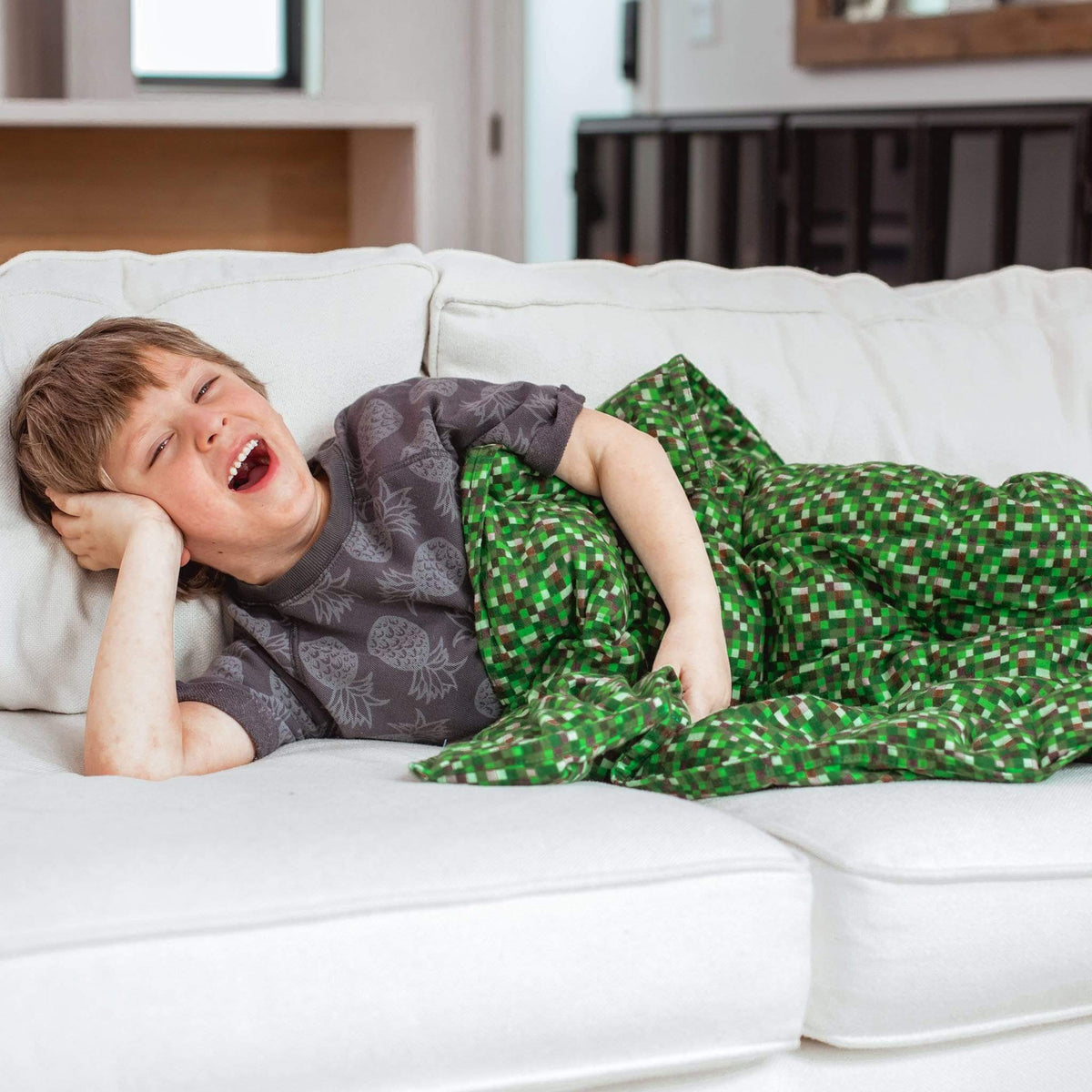Little boy relaxed on a white couch under his Minecraft Flannel Weighted Blanket