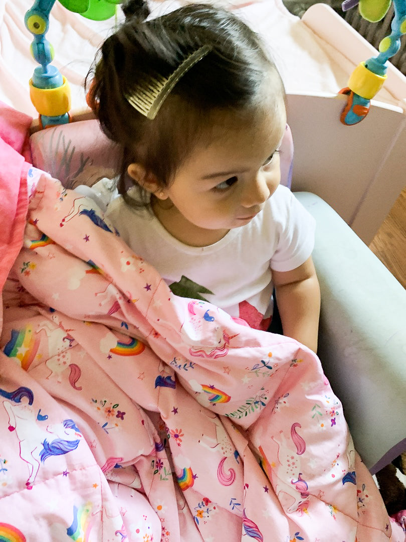 Little girl snuggles under her Unicorn Weighted Blanket Close up of the pink pattern